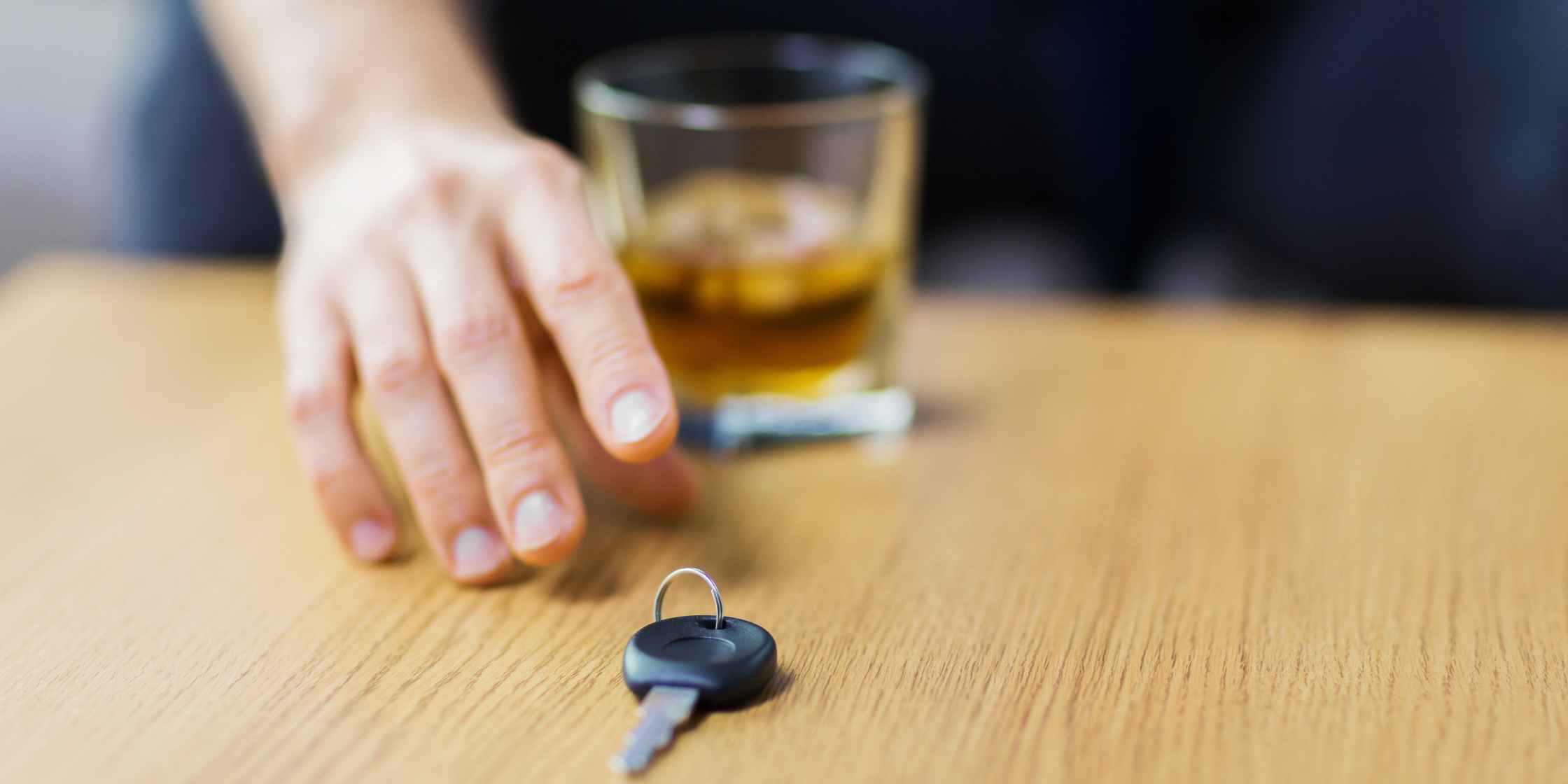 navigating-DUI-charges-in-colorado Close-up of a hand reaching for a glass of alcohol with car keys nearby, representing DUI risk.