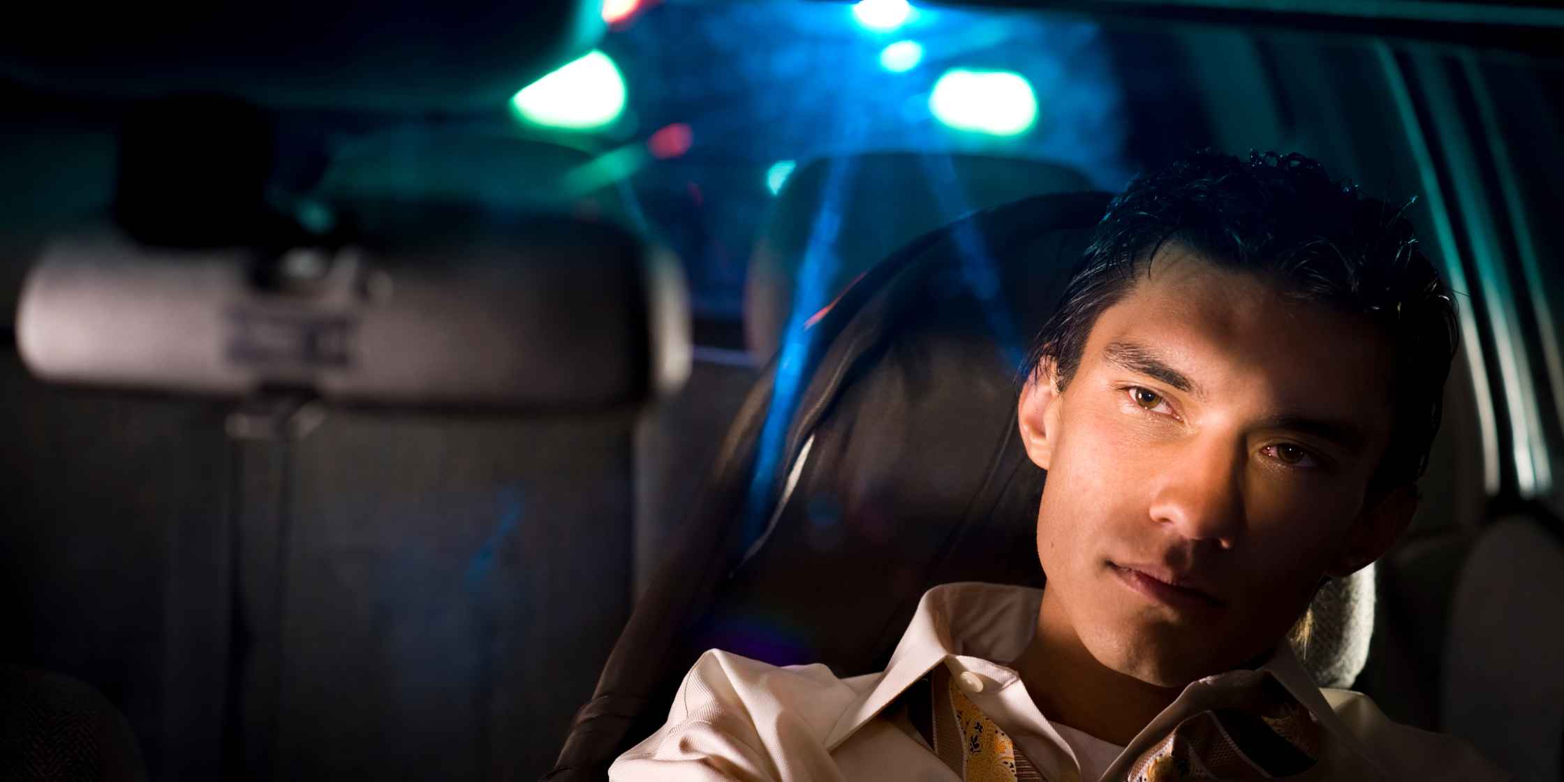 The Top 3 Myths About DUI in Colorado Man in car at night with police lights reflecting in rearview mirror, related to DUI myths in Colorado