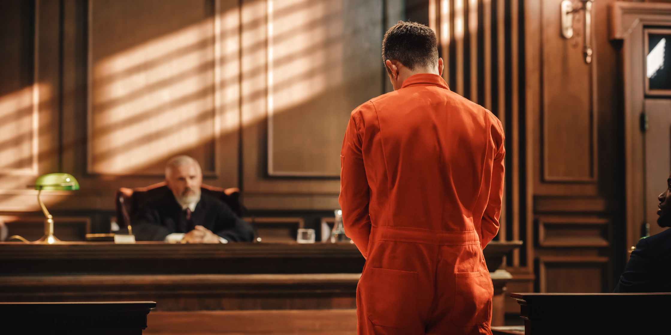 Defendant in orange jumpsuit standing before judge in courtroom during criminal case. Criminal Defense Attorney Colorado Springs - Maher and Maher Law